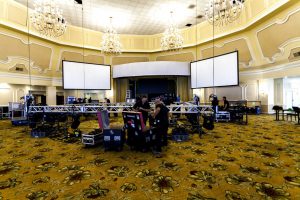 A large conference room with chandeliers, three video walls and a lighting rig in the center being set up.